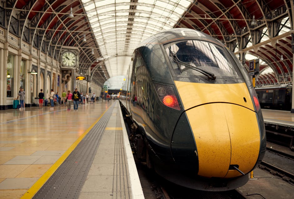 Interior view of Paddington Station with a modern high-speed train positioned on the platform. The station features an arched glass and metal roof allowing natural light to illuminate the polished stone floor. On the platform, passengers with luggage are waiting, some seated and others walking, while the station’s historic clock hangs above the platform. Paddington Carpet Cleaning's professional staff are not visible in this image, but the setting highlights the importance of maintaining clean, hygienic environments in transport hubs through expert cleaning and sanitisation services. The platform surface appears clean, dry, and well-maintained, emphasizing the importance of surface cleaning for hygiene and safety.
