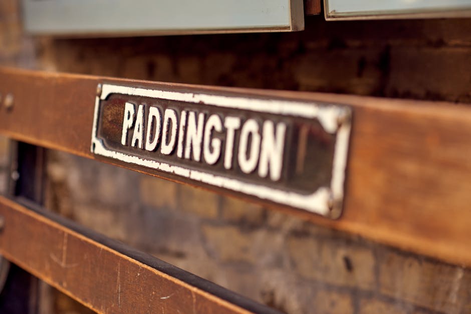 A close-up view of a vintage wooden surface, featuring a rusted metal nameplate with the word 'PADDINGTON' painted in white uppercase letters. The wooden slats beneath are stained and weathered, indicating age and exposure. The scene is illuminated with soft, natural lighting highlighting the textures of the aged wood and metal. The setting suggests an outdoor or semi-outdoor environment, possibly part of a transport or signage fixture. This image exemplifies surface cleaning and maintenance practices, which Paddington Carpet Cleaning offers for safeguarding the appearance and hygiene of surfaces in commercial or public spaces, aligning with their deep cleaning and sanitisation services near Paddington Station for commuters.